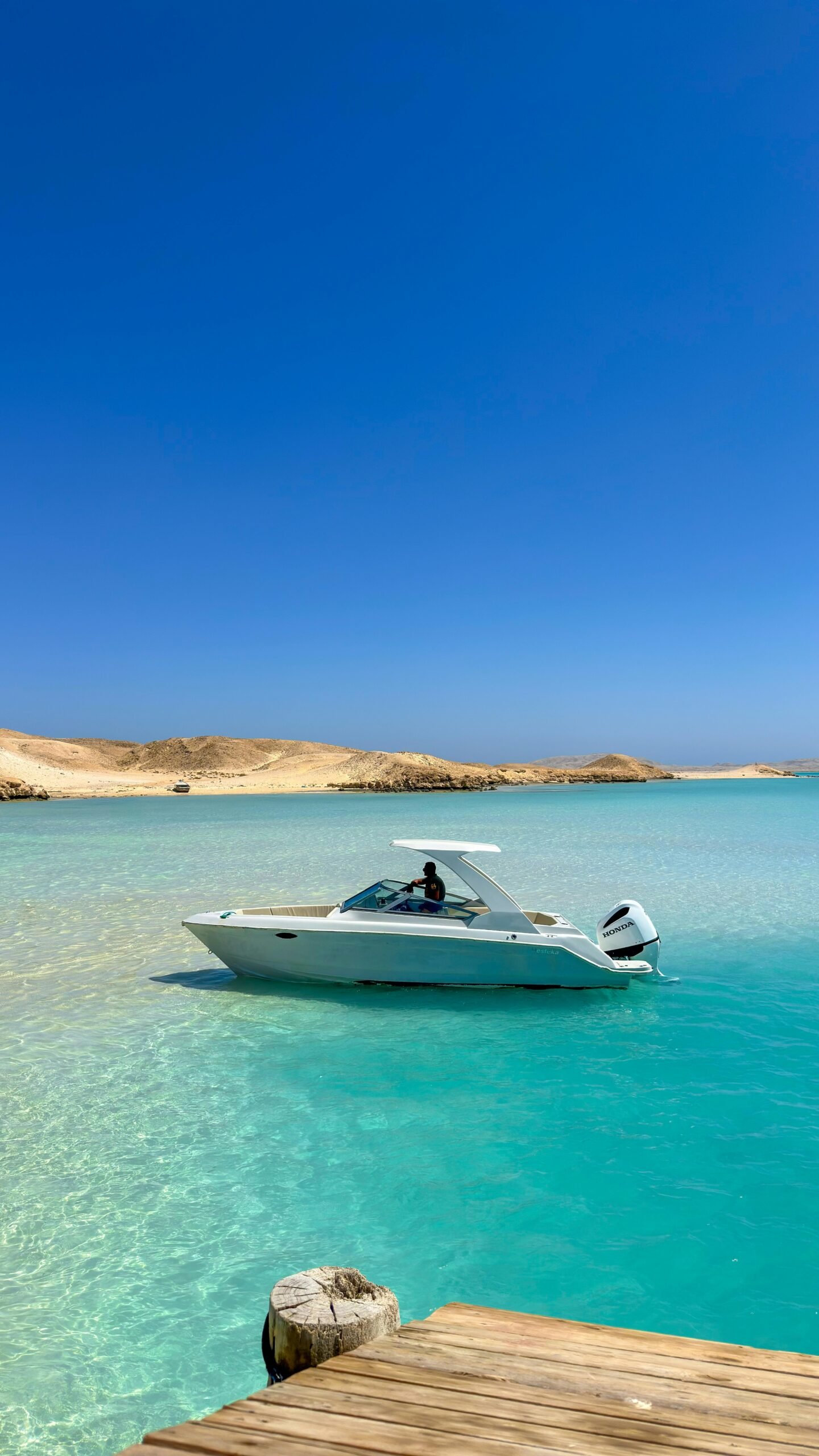 A white motorboat on the clear waters of the Red Sea under a vibrant blue sky, near sandy shores.